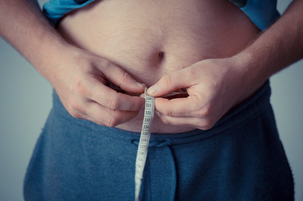 Overweight man holding measuring tape around waist