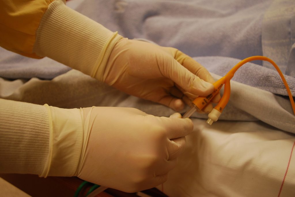 Gloved hands holding a catheter at hospital bed