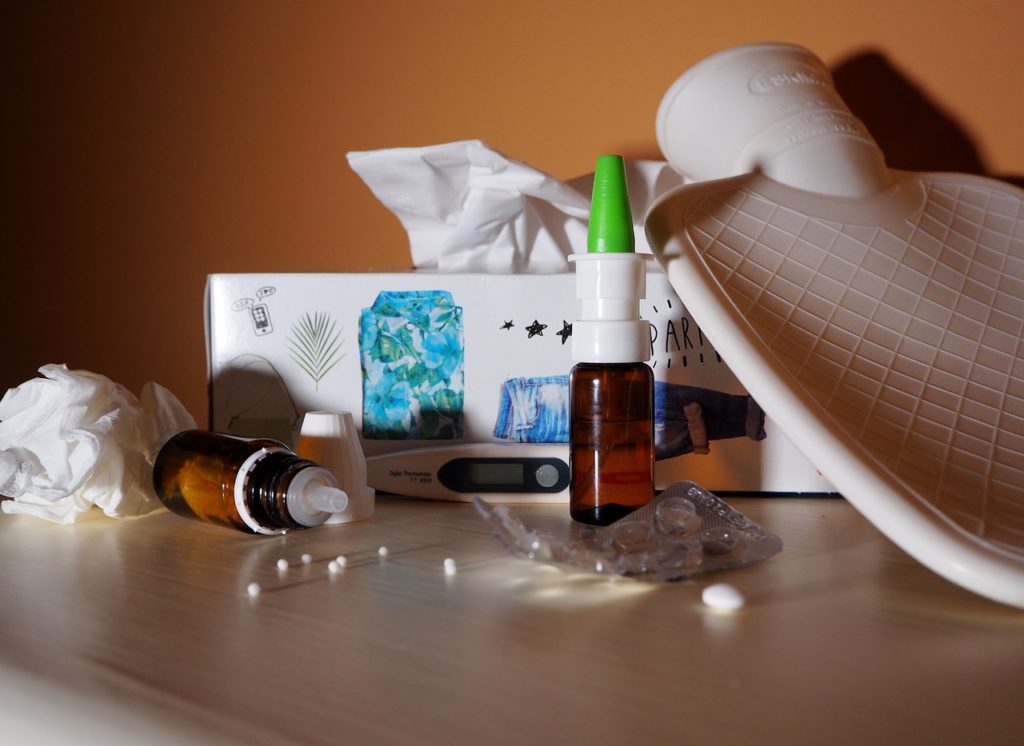 Flu medication, tissue box, hot water bottle, tablets scattered on desk